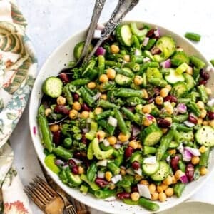 Three bean salad in a white serving dish with silver serving spoons.