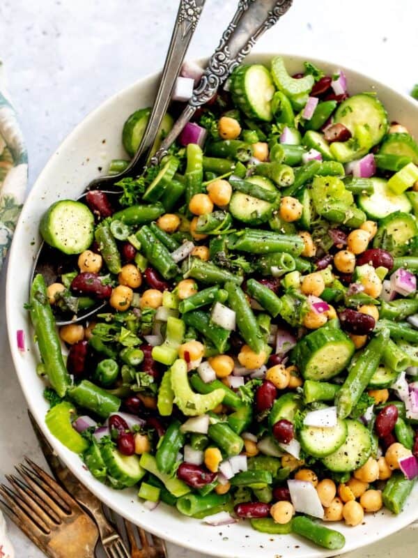 Three bean salad in a white serving dish with silver serving spoons.