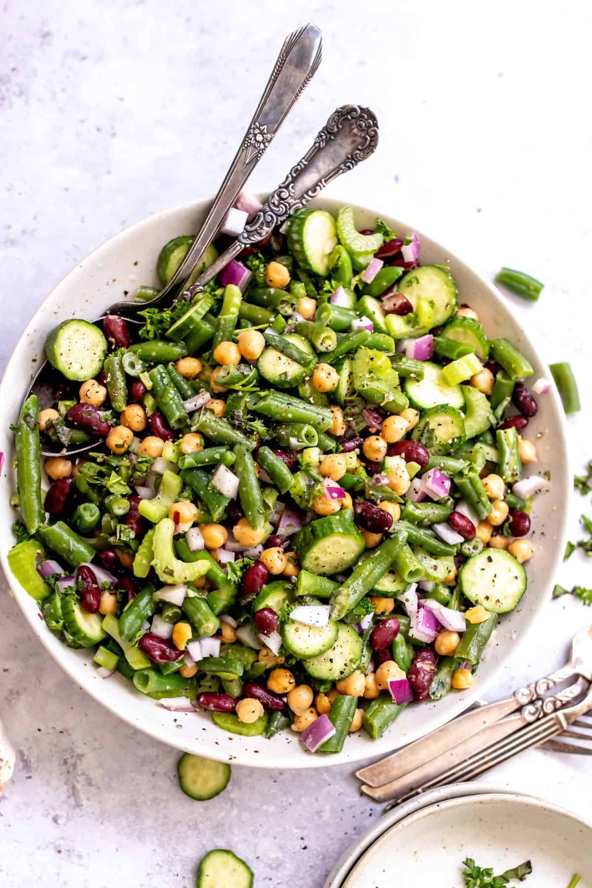 Three bean salad in a white serving dish with silver serving spoons.