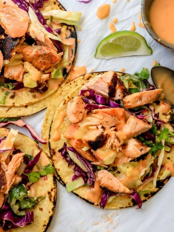 Bang Bang Salmon Tacos on parchment paper with limes on the side.