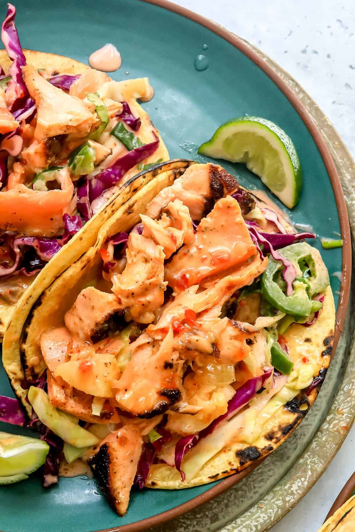 Bang Bang Salmon Tacos on a green plate with sauce and a squeezed lime. 