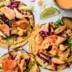 Bang Bang Salmon Tacos on parchment paper with limes on the side.