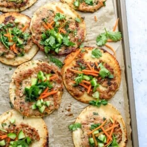 Dumpling tacos on a baking sheet with toppings and sauce.