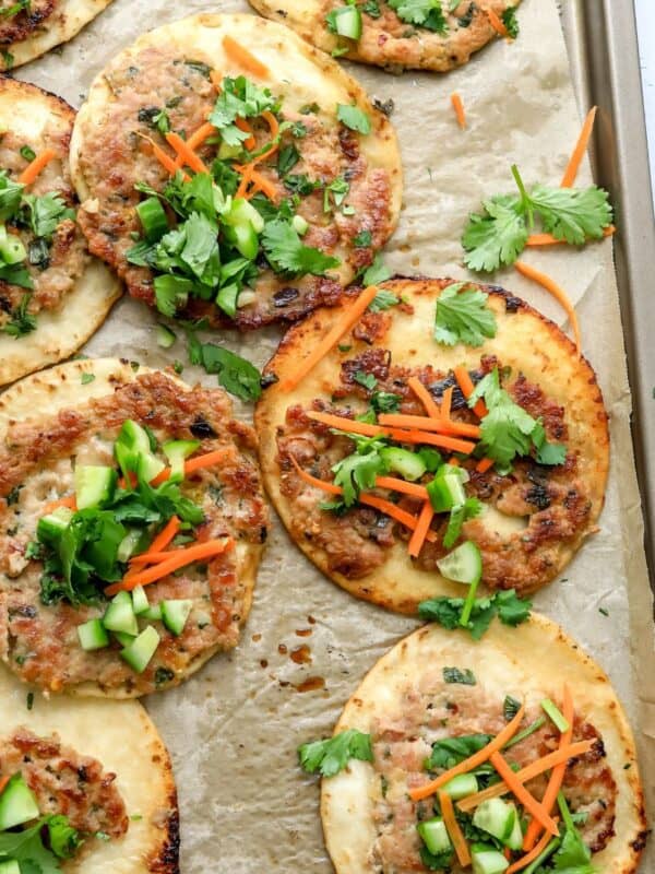 Dumpling tacos on a baking sheet with toppings and sauce.