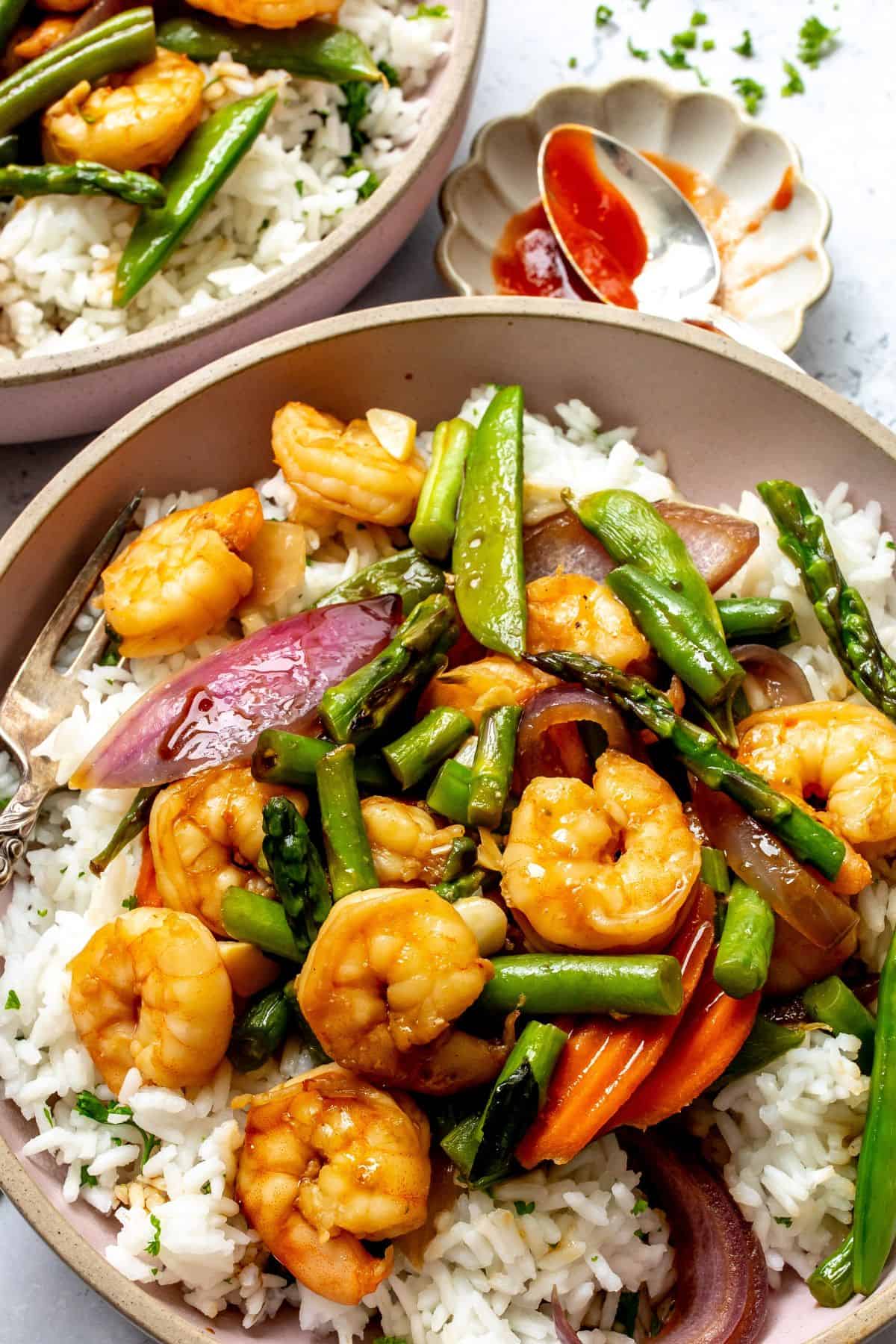 Garlic shrimp stir fry served over white rice in pink bowls with forks to the side up close. 