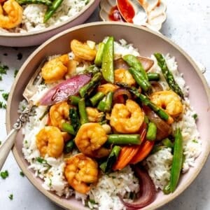 Garlic shrimp stir fry served over white rice in pink bowls with forks to the side.