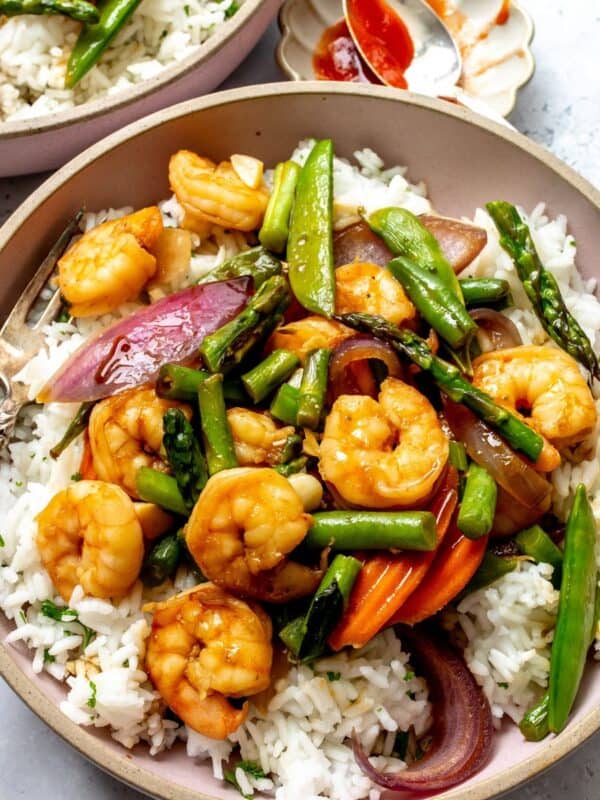 Garlic shrimp stir fry served over white rice in pink bowls with forks to the side.