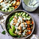 Grey bowls with chicken power bowls in them and dressed with sauce.