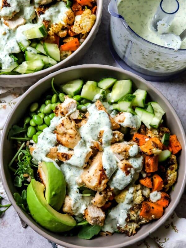 Grey bowls with chicken power bowls in them and dressed with sauce.
