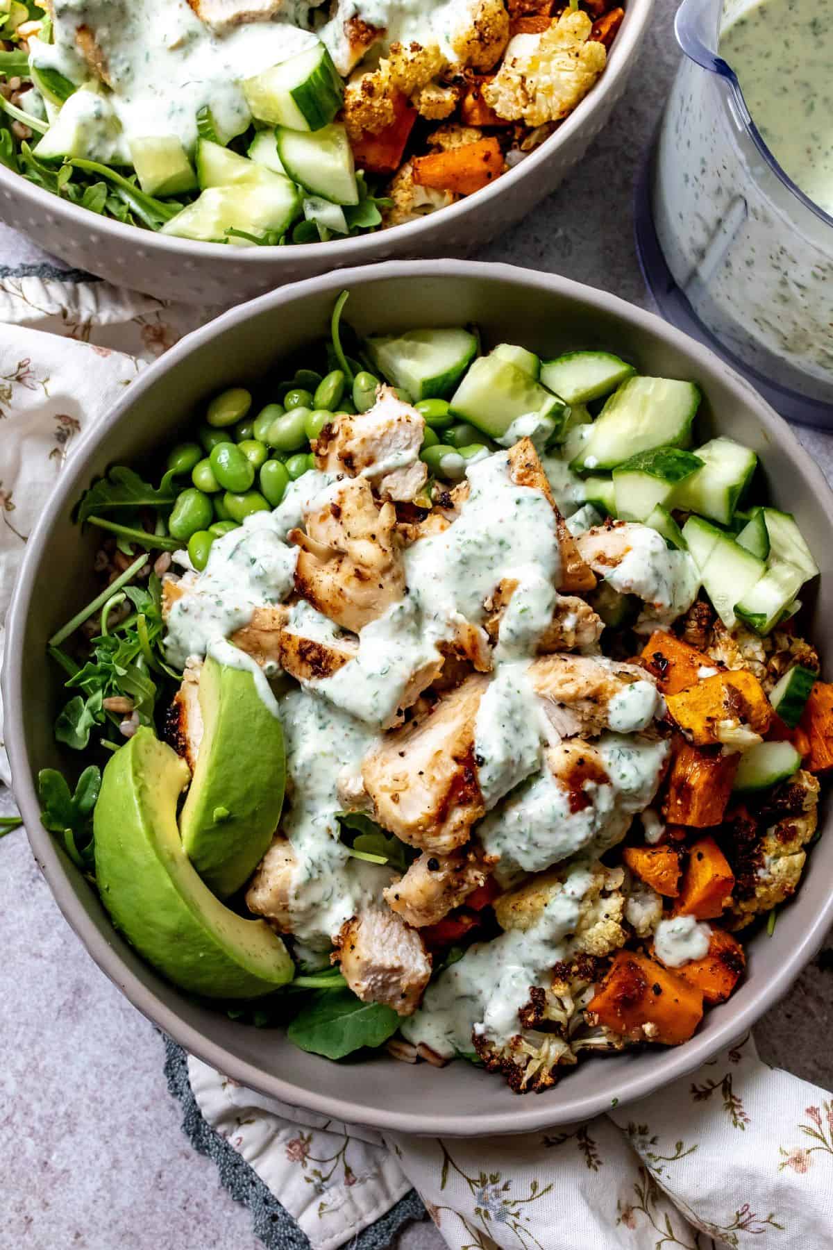Grey bowls with chicken power bowls in them and dressed with sauce.