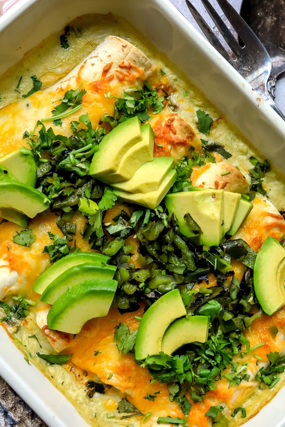Poblano Chicken Enchiladas in a baking dish with avocados and peppers on top.