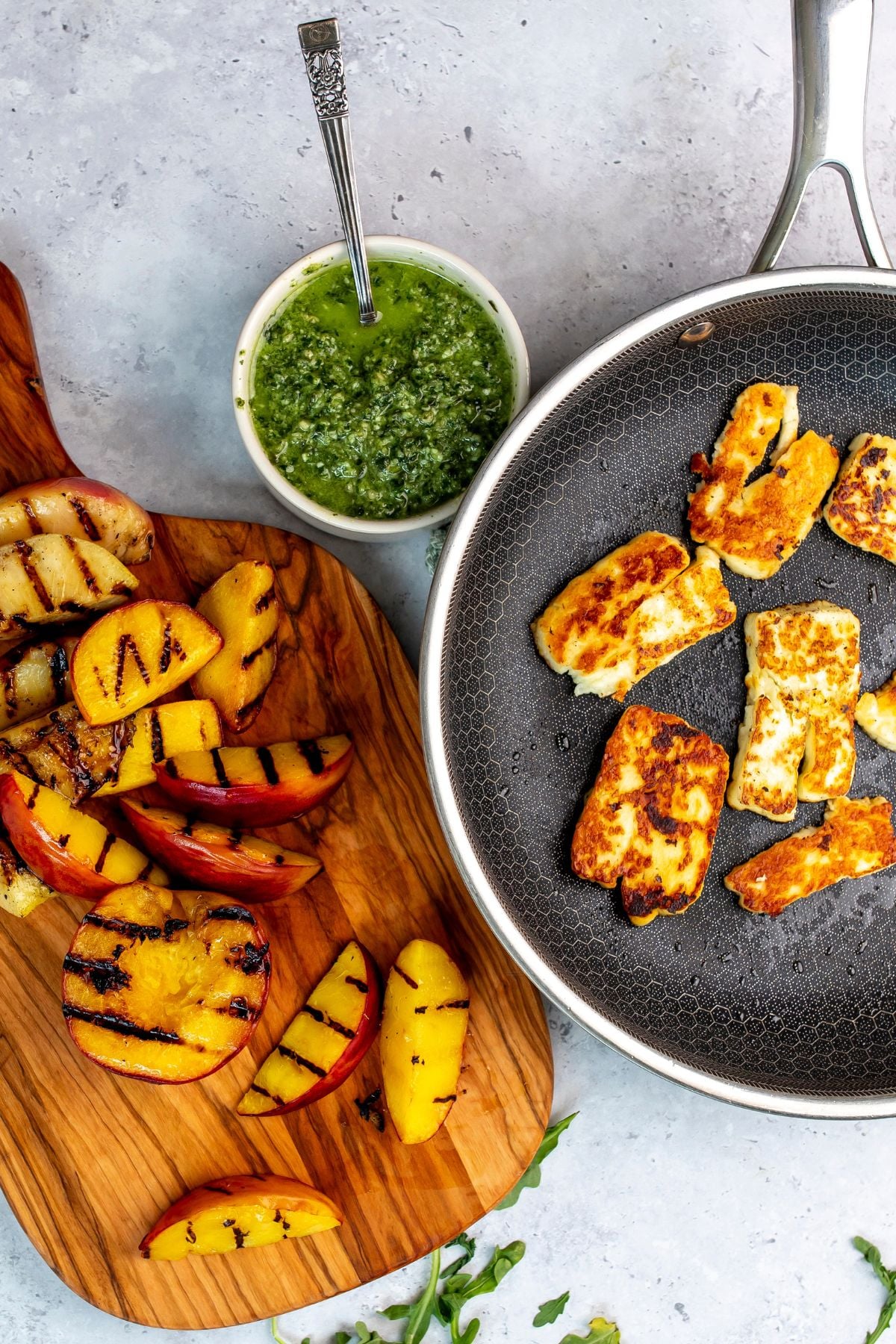wood cutting board with peaches on it and arugula to the side.