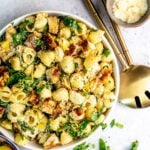 Lemon basil pasta salad in a white bowl with gold serving utensils to the side.