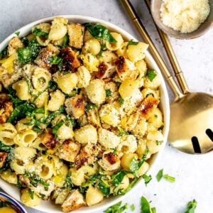 Lemon basil pasta salad in a white bowl with gold serving utensils to the side.
