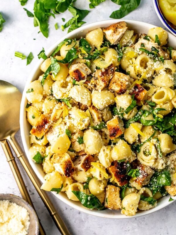 Lemon basil pasta salad in a white bowl with gold serving utensils to the side.