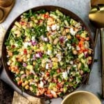 Brown ceramic bowl full of white bean salad with dressing to the side and chips for dipping.