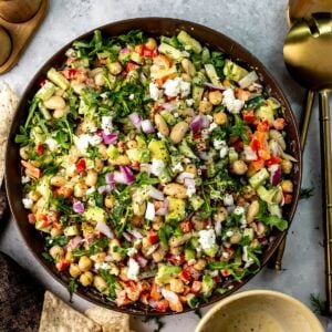 Brown ceramic bowl full of white bean salad with dressing to the side and chips for dipping.