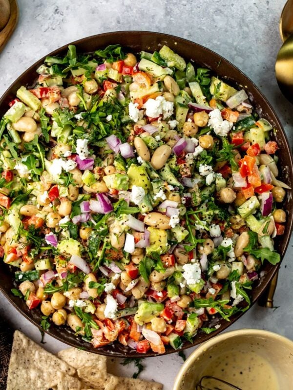 Brown ceramic bowl full of white bean salad with dressing to the side and chips for dipping.