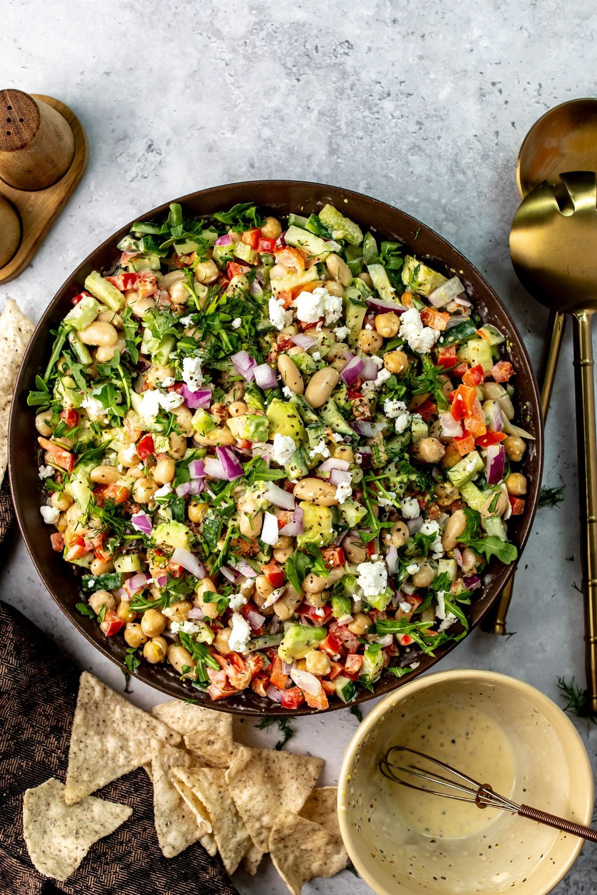 Brown ceramic bowl full of white bean salad with dressing to the side and chips for dipping.