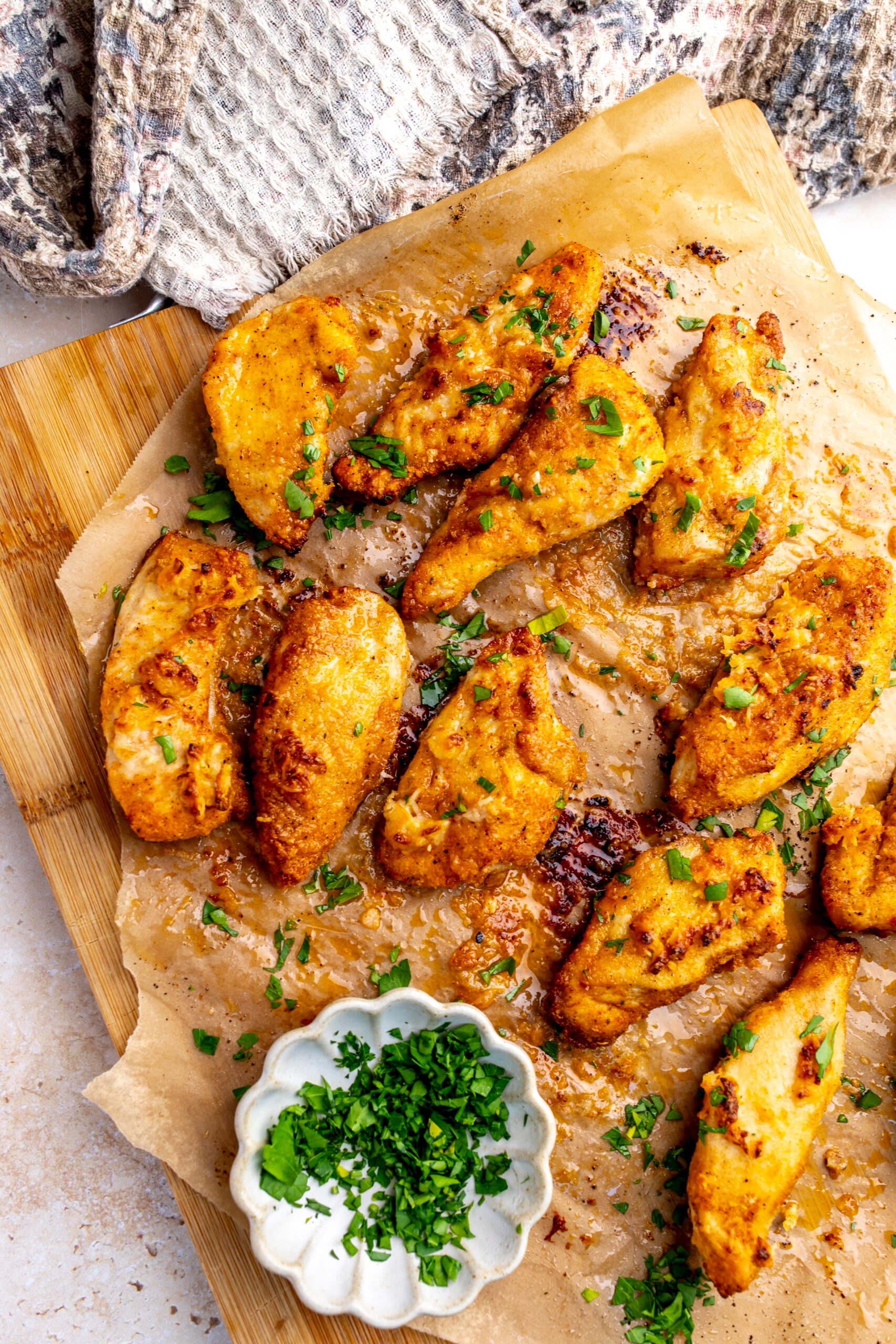 Golden Garlic Parmesan Chicken Strips on brown parchment paper with parsley on top.