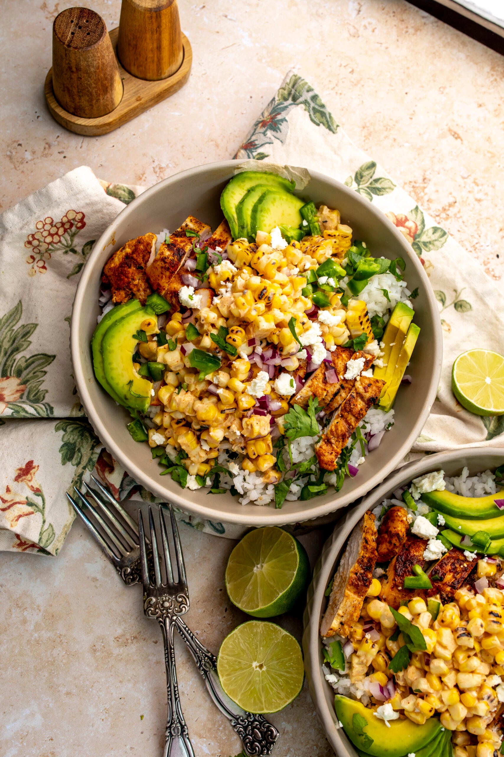 Street Corn Chicken Rice Bowls in a grey textured bowl. Limes on the side with forks.