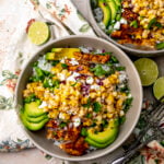 Two Chicken Street Corn Rice Bowls on a counter with a floral napkin underneath and silver forks to the side.
