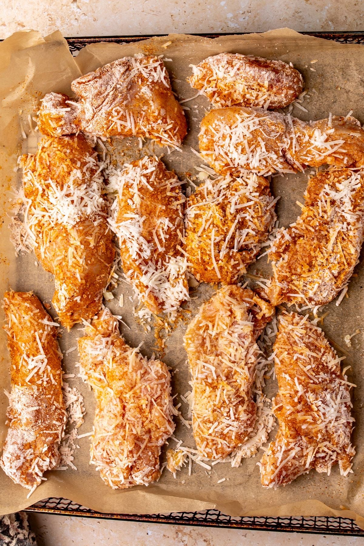 Chicken strips with coating and Parmesan cheese on top on parchment paper.