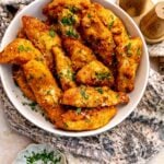 Golden Garlic Parmesan Chicken Strips in a white bowl topped with parsley.