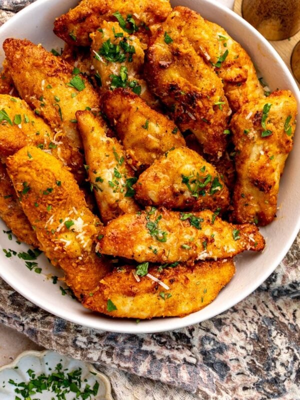Golden Garlic Parmesan Chicken Strips in a white bowl topped with parsley.