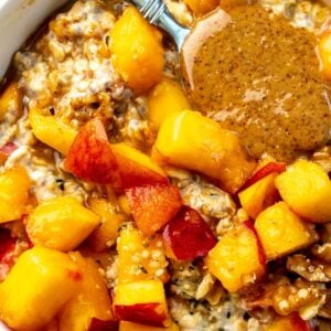 A spoon with almond butter on it rests in a bowl of peach overnight oats.