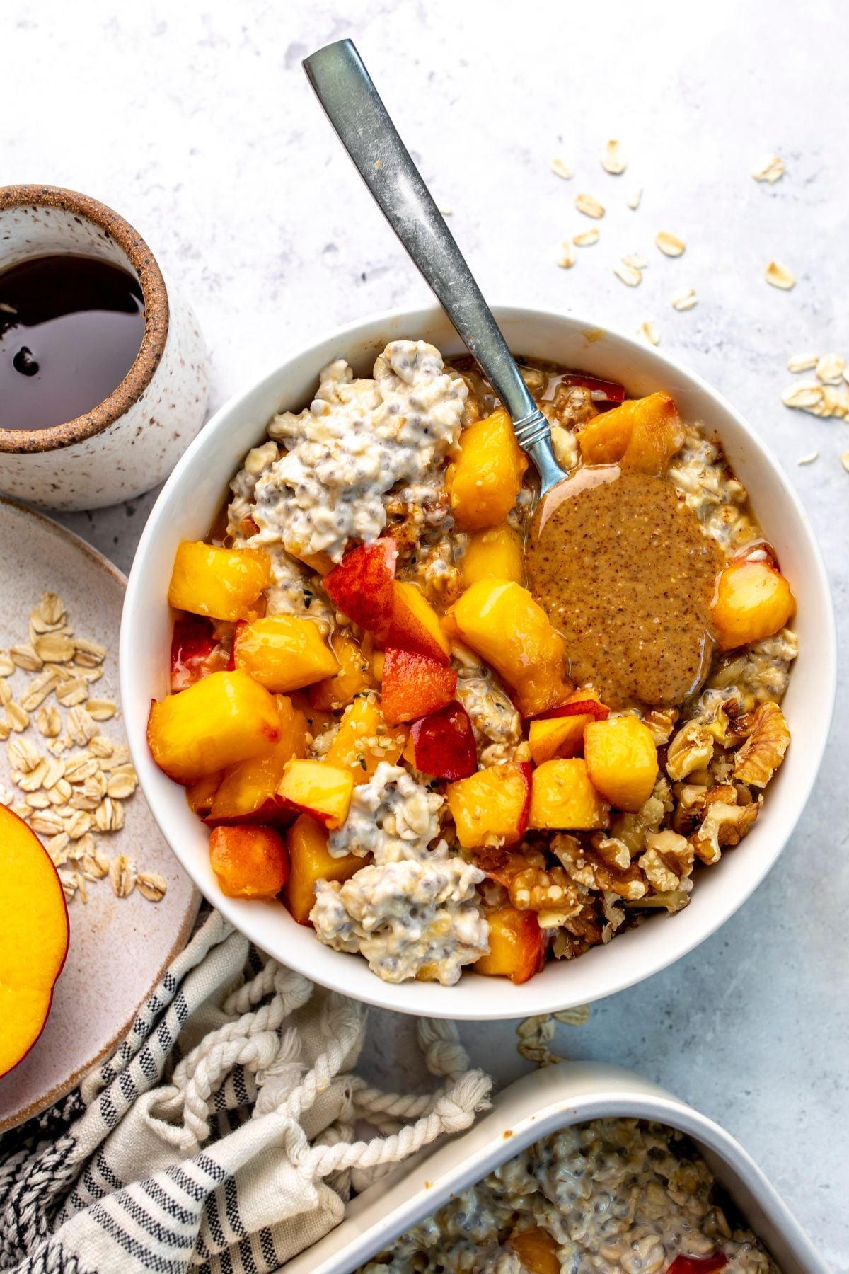 A bowl of peach overnight oats sits on a countertop with a spoon sitting in the bowl.
