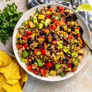 Beautiful black bean rice salad in a white bowl with a silver spoon and chips to the side.