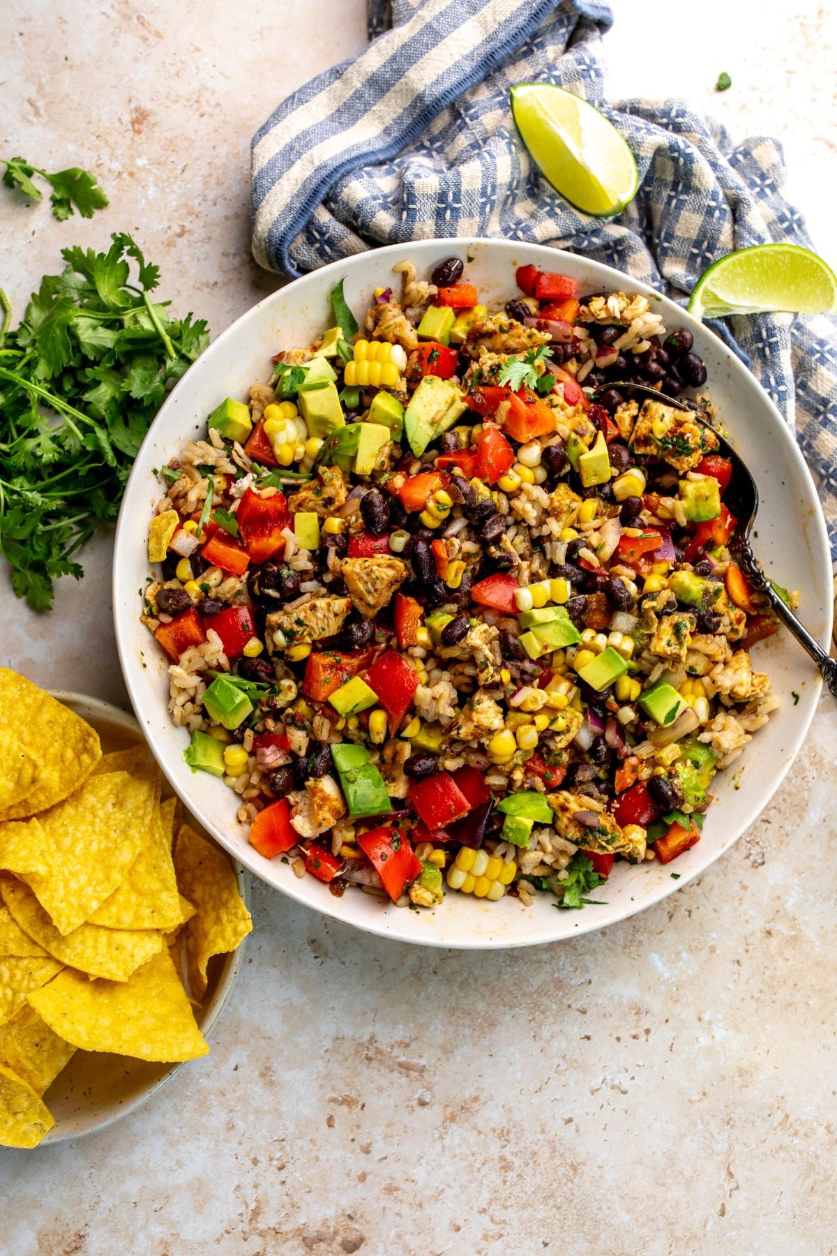 Beautiful black bean and rice salad in a white bowl with a silver spoon and chips to the side.