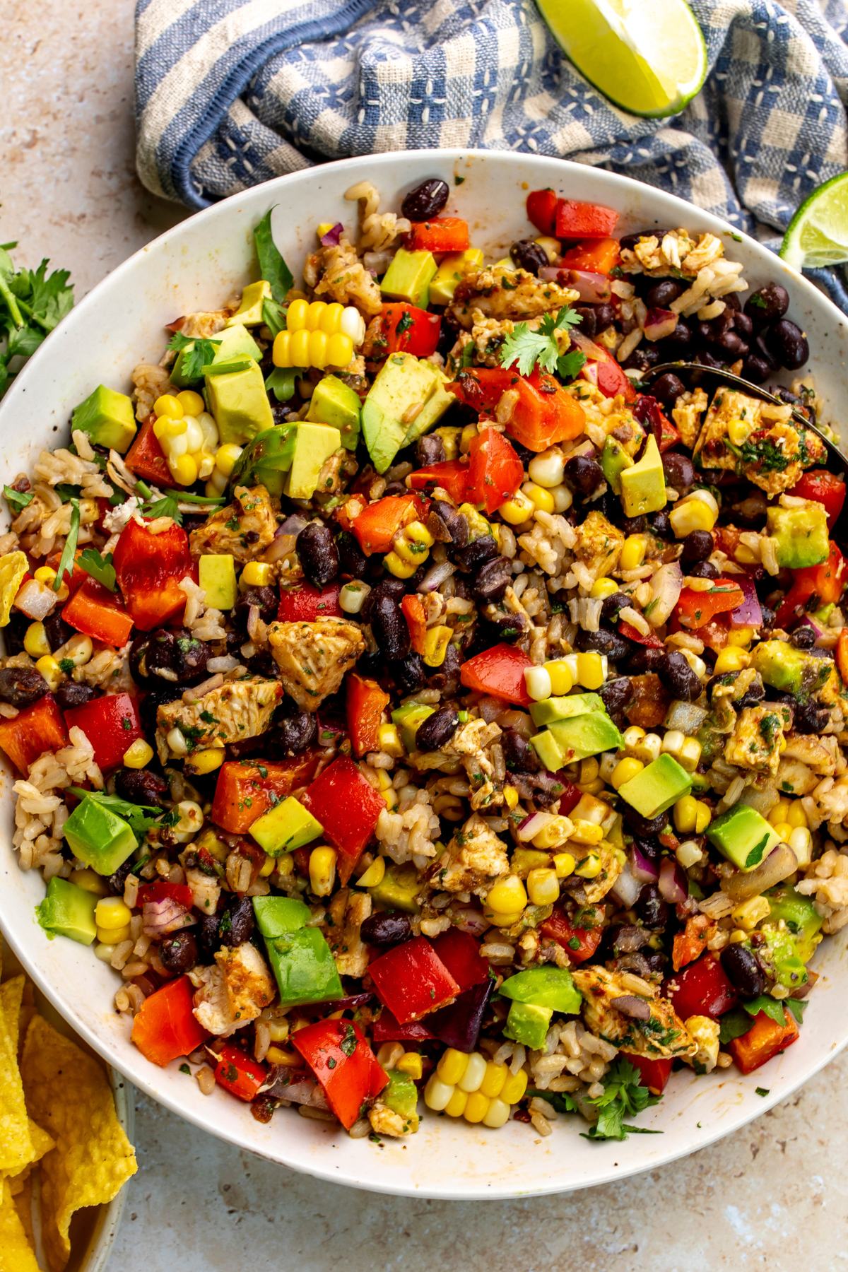 Beautiful black bean rice salad in a white bowl with a silver spoon and chips and lime to the side.