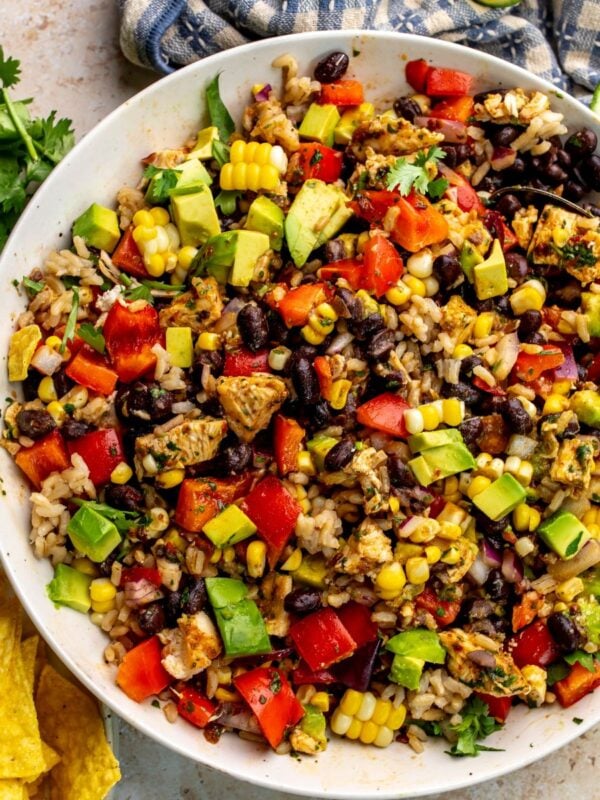 Beautiful black bean rice salad in a white bowl with a silver spoon and chips to the side.