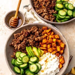 Two hot honey ground beef bowls on a countertop with a small bowl of hot honey on the countertop next to the bowls.