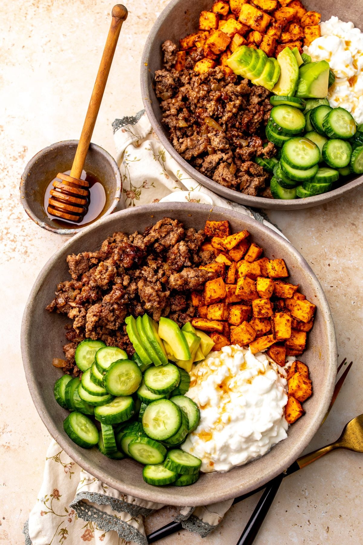 Two hot honey ground beef bowls on a countertop with a small bowl of hot honey on the countertop next to the bowls.