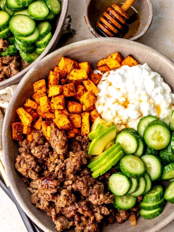 Hot honey ground beef bowls with sweet potatoes, avocado, cucumbers, and cottage cheese in a bowl on a countertop.