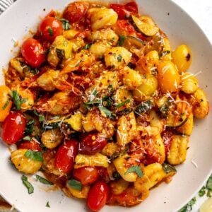 Blistered tomato pasta gnocchi in a white bowl with basil on top.