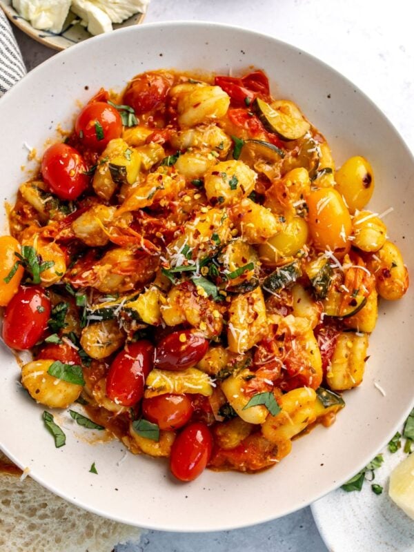 Blistered tomato pasta gnocchi in a white bowl with basil on top.