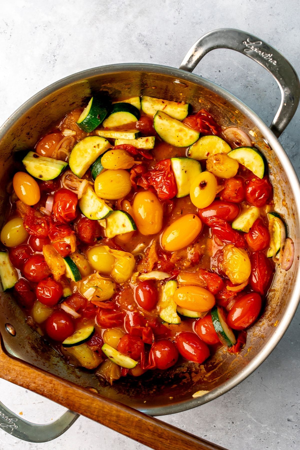 Large silver skillet with blistered tomatoes in it and wooden spoon to the side.