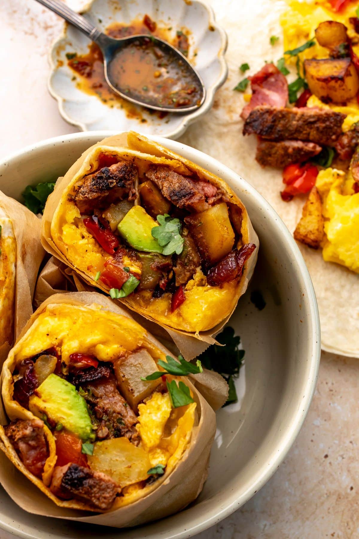 Two steak breakfast burritos in a bowl on a countertop.