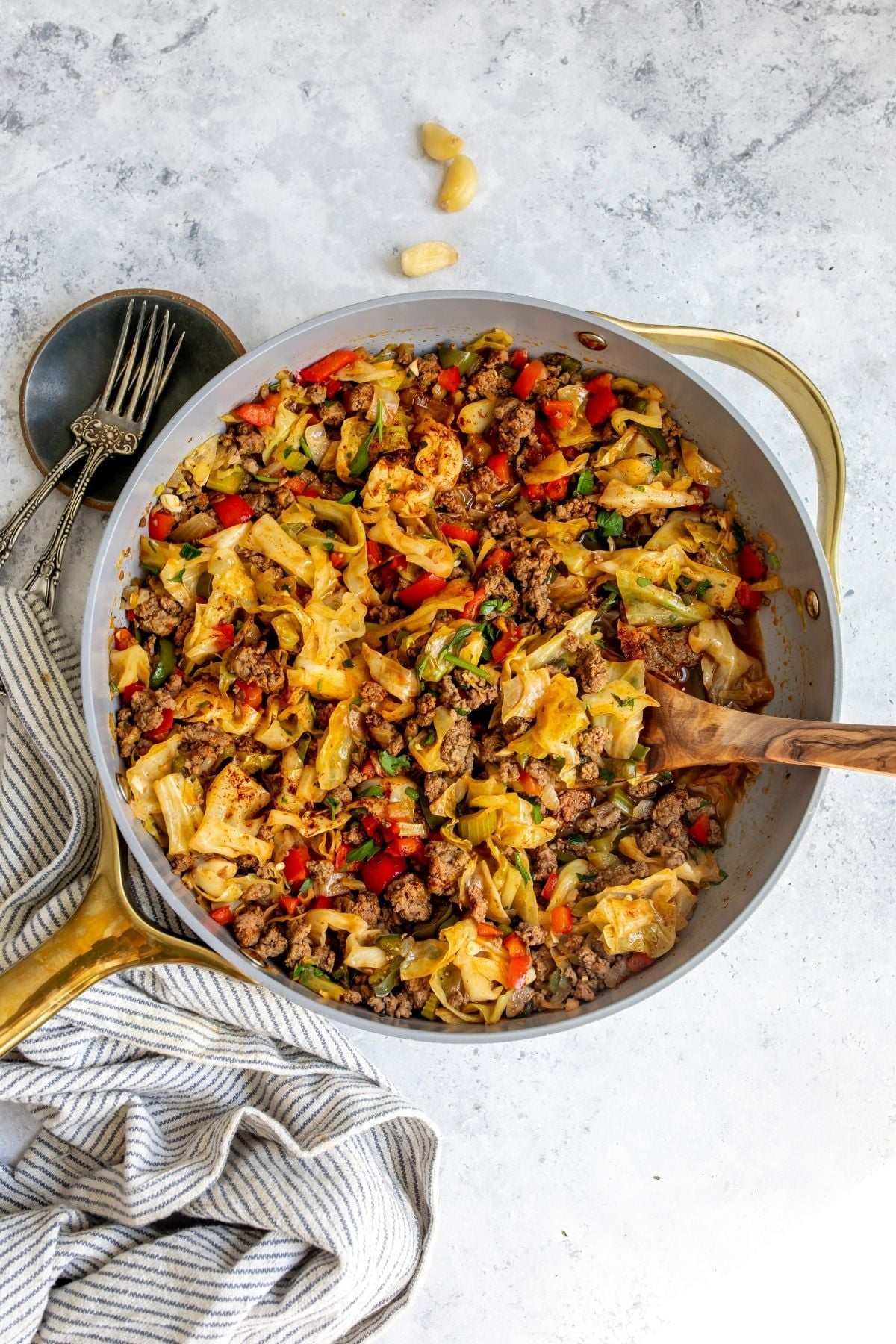 Dirty cabbage in a grey pan with a wooden spoon and a towel to the side.
