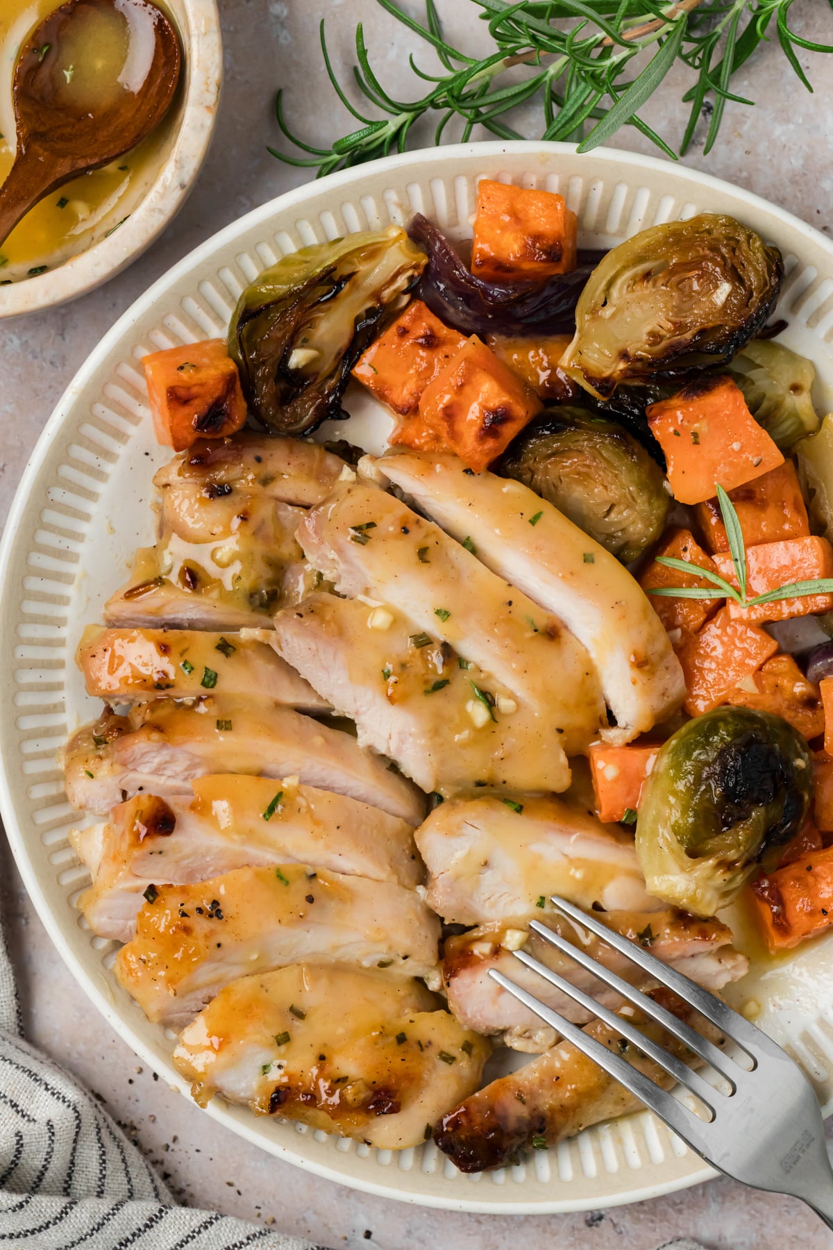 The sliced chicken thighs on a plate with the roasted brussels sprouts and sweet potato for serving.