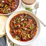 Slow cooker birria in a white bowl on a countertop garnished with chopped cilantro and onion.