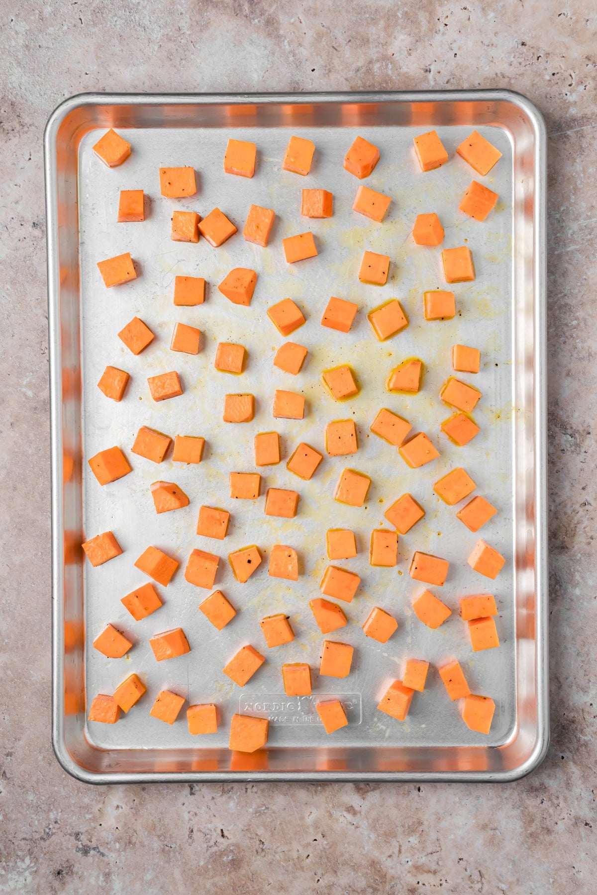 The cubed sweet potatoes tossed in the olive oil on a sheet pan before baking.