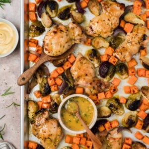 Maple dijon sheet pan chicken thighs on a sheet pan with roasted sweet potatoes and brussels sprouts.
