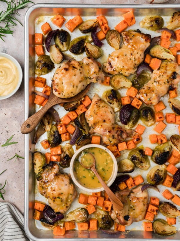 Maple dijon sheet pan chicken thighs on a sheet pan with roasted sweet potatoes and brussels sprouts.