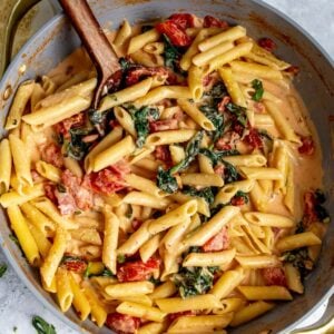 Creamy Tomato Spinach Pasta in a grey skillet with a spoon.