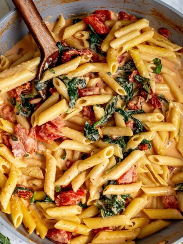 Creamy Tomato Spinach Pasta in a grey skillet with a spoon.